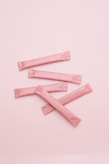 Pink sugar stick pouches scattered on pink background. Sweet snack or beverage additive.