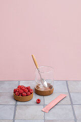Bowl with fresh red raspberries next to an empty glass and an unopened pink stick pack.