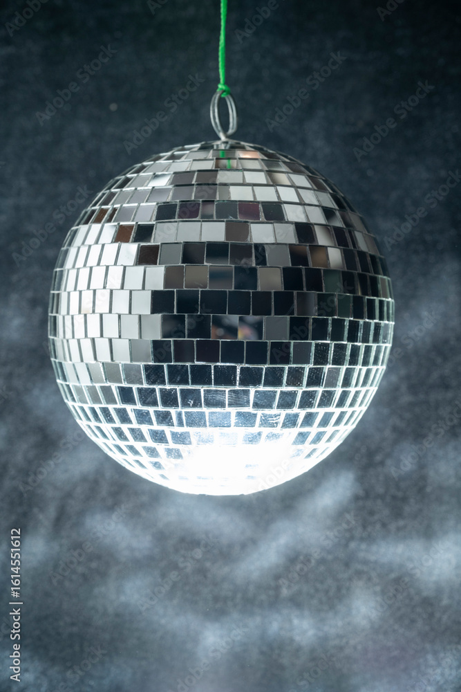 Poster disco ball hanging is comprised of small mirrors and has a light reflecting on it for a party effect
