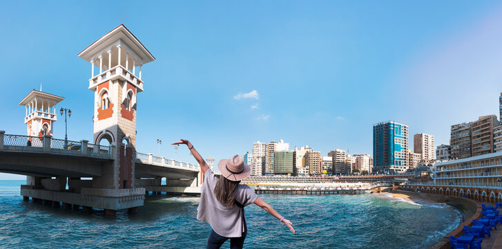 Happy woman in hat open arms in free happiness standing and posing - People walk the Stanley Bridge, popular landmark of Alexandria, Egypt - Powered by Adobe