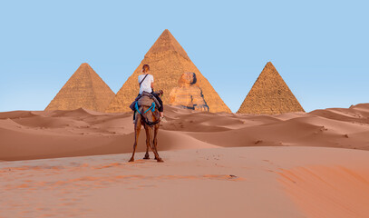 Fototapeta premium Camels in Giza Pyramid Complex - A woman in a red turban riding a camel across the thin sand dunes - Cairo, Egypt