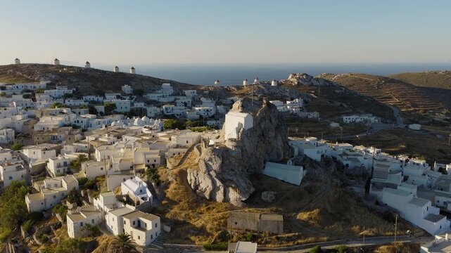 Aerial orbit around the medieval Castle of Amorgos in Chora during sunrise. The iconic Cycladic windmills create a timeless island backdrop