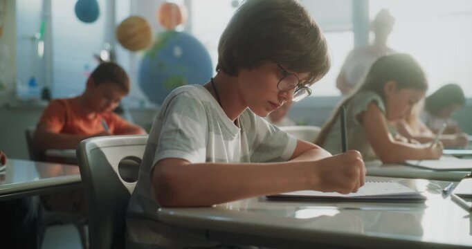 Primary School Children Writing School Test, Doing Tasks in Notebooks. Female Teacher Walking Between Desks, Controlling Group of Diverse Kids During the Exam Process in Modern Classroom. Dolly Shot.