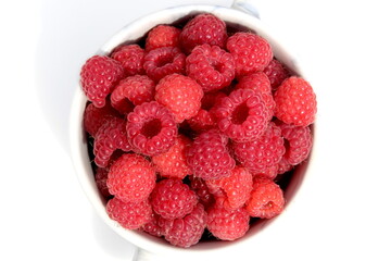 On a white background there is a plate with ripe juicy raspberries.	