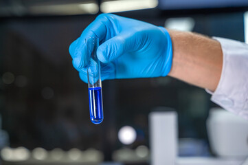 Close up unknown lab technician with blue gloves holding fluid test tube working in laboratory