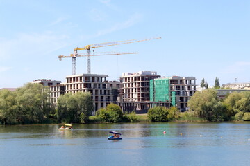 On the shore of the reservoir there is a city with tall buildings and working construction sites.