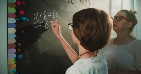 Talented Boy Demonstrating Math Knowledge: Close Up Shot of Primary School Student Solving Mathematical Equation Writing on the Board with Chalk in Classroom. Female Teacher Checking Correct Answers. - Powered by Adobe