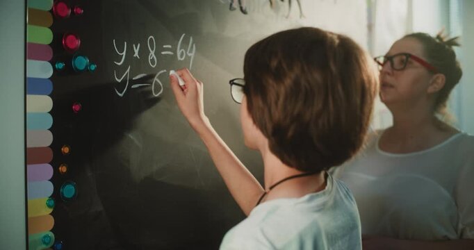 Talented Boy Demonstrating Math Knowledge: Close Up Shot of Primary School Student Solving Mathematical Equation Writing on the Board with Chalk in Classroom. Female Teacher Checking Correct Answers.