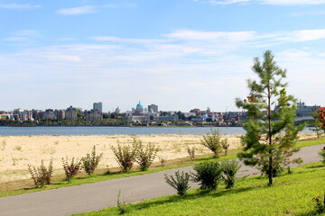 View of the city with houses and trees on a sunny hot summer day from a sandy beach.