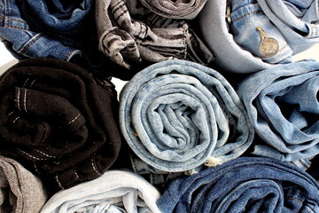 The denim pants are rolled up and laid on top of each other.