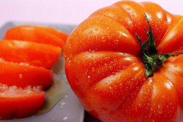 Ripe, juicy tomatoes, whole and sliced, glistening with water droplets, presented on a gray surface