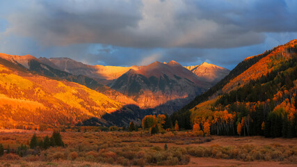Scenic autumn landscape with Autumn trees against mountain peak and cloudy sky in San Juan under evening light.