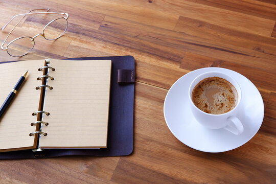 ミルクをたっぷり入れたコーヒー、カフェ・ラッテを飲みながら、システム手帳でデスクワーク中のイメージ
