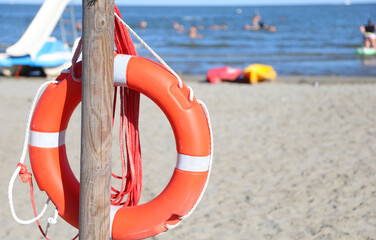 orange life jacket made of sturdy plastic hanging on a wooden pole on the sandy beach available to lifeguards to rescue people