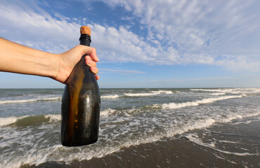 hand of the person found bottle on seashore with secret message or pirate treasure map inside