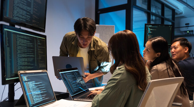 Asian man presents code during a software development meeting or coding workshop, guiding attendees through problem-solving and programming concepts in an educational setting.