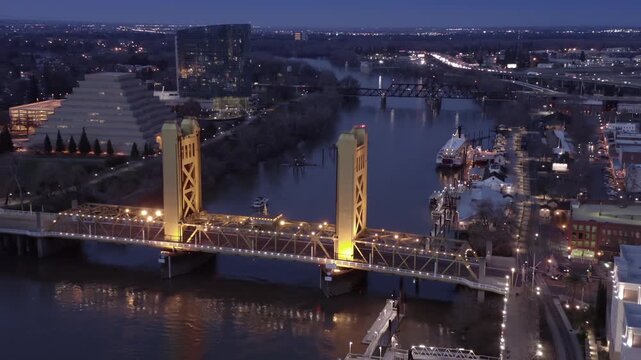 The Tower Bridge spans the Sacramento River at dusk, connecting the city. The iconic yellow bridge is a landmark in Sacramento, California, USA.