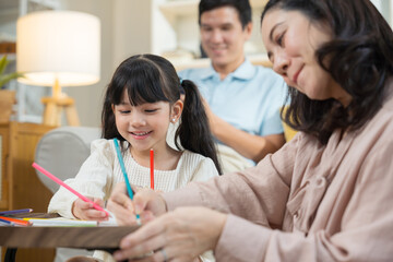 Asian mother and daughter happily sit together in the living room, drawing pictures and enjoying...