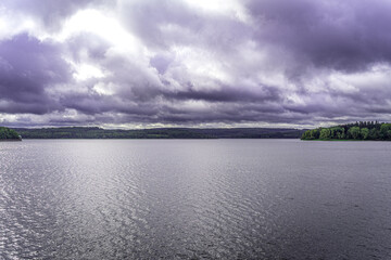 Der Möhnesee zeigt sich von seiner dramatischen Seite – dunkle Wolken ziehen über das Wasser, das Licht bricht sich in der Fläche, während am Horizont das Grün der Wälder leuchtet.