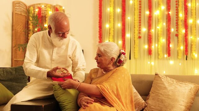 Senior indian husband give surprise gift of gold bangles to wife on diwali festival or marriage anniversary occasion. Retired Elderly couple Deepavali celebration. 4k