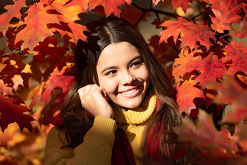 Autumn kid girl face on autumn fall leaf background. cheerful teen girl standing at beautiful autumn leaves