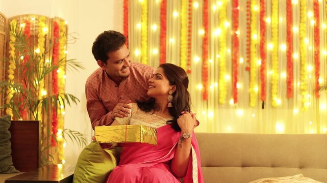 Young indian husband give surprise gift to wife on diwali festival or marriage anniversary occasion. Deepavali celebration. 4k