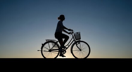 Obraz premium A person riding a bicycle against a gradient sky captured in a striking silhouette against the horizon