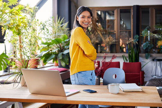 Happy businesswoman standing with arms crossed at desk in loft office