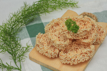 Close-up of crispy Indonesian rice crackers known as rengginang, served on a wooden board with rustic background. Traditional local snack made from glutinous rice, deep-fried to golden crisp.
