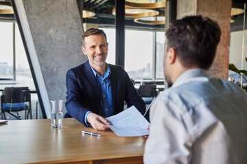 Happy recruiter giving employment contract to candidate at desk