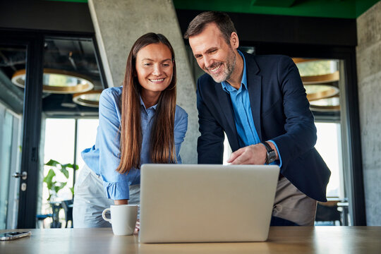 Smiling mature businessman discussing over laptop with businesswoman at desk