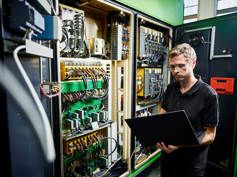 Technician using laptop at machine in modern factory