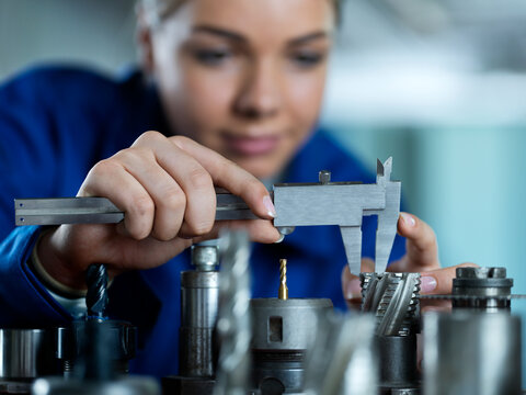 Trainee measuring CNC tool with caliper in factory
