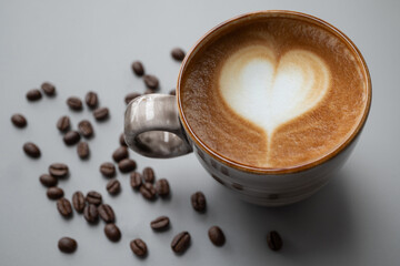 Heart shape Latte art in a ceramic cup  place on gray background  with copy space left, there are coffee beans around
