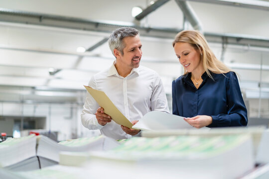 Smiling businessman discussing with colleague reading documents in factory
