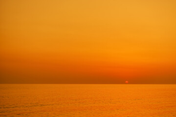 Sunset over the sea, golden shades of the sun in the haze after smoke or smog on the horizon, fantastic view of the evening sea
