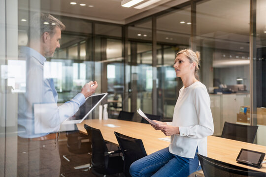 Businessman and businesswoman with digital tablet and documents talking in office