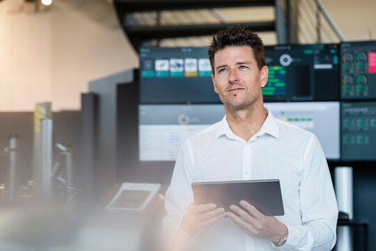 Smiling businessman holding tablet PC in front of computer monitors