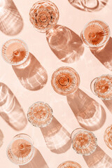 Minimal summer party concept, glasses of rose wine or champagne on pink with shadows and light reflections. Bright shine wineglass with sparkling alcohol drink at sunlight, top view monochrome pattern