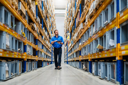 Manager taking inventory walking in warehouse