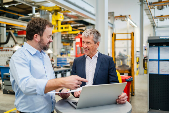 Manager pointing at laptop by businessman at factory