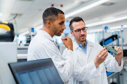 Two colleagues discussing over motherboard in electronics factory