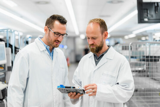 Technicians in white lab cots disussing over electronic component