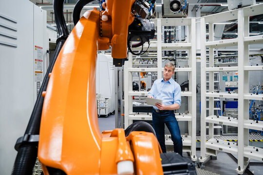 Businessman using digital tablet at industrial robot in a factory