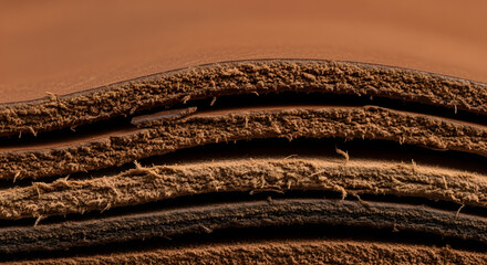 Textured layers of brown leather material in a dynamic, undulating stack, showing a detailed fibrous cross-section