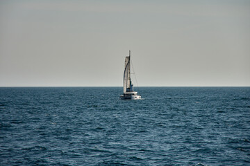 A sailing boat crossing the Vigo Estuary next to a lighthouse with the open sea and a clear sky on a peaceful sailing day