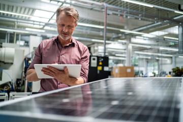 Businessman using tablet PC standing near solar panel at factory