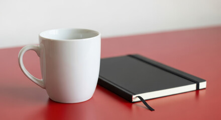 White Mug with Black Notebook and Pen on Red Table for Office Workspace Productivity Marketing or Study Blog Visual