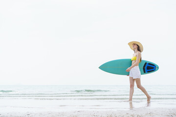 Beautiful slim fit caucasian woman walks on the beach with surfboard. Summer activities and...