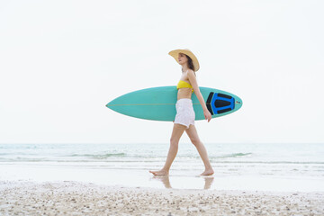 Beautiful slim fit caucasian woman walks on the beach with surfboard. Summer activities and...